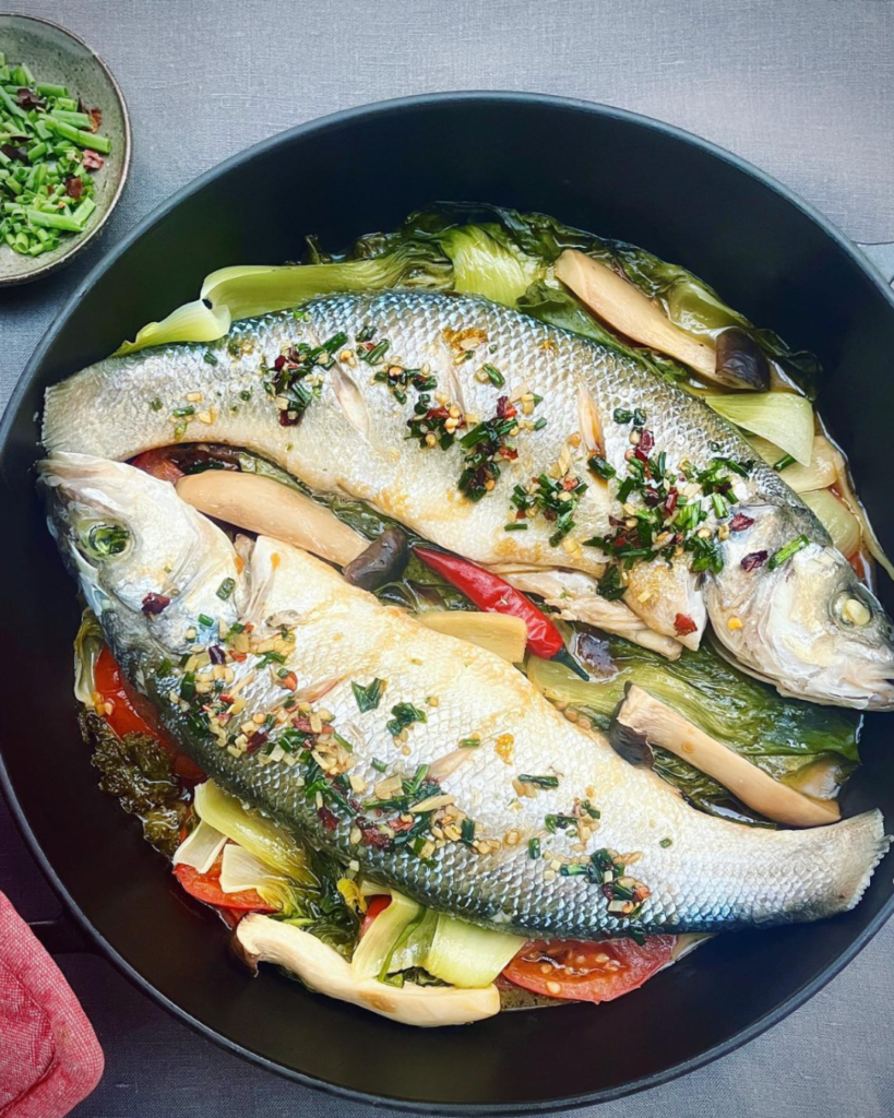 Two whole sea bass in a casserole over colorful vegetables