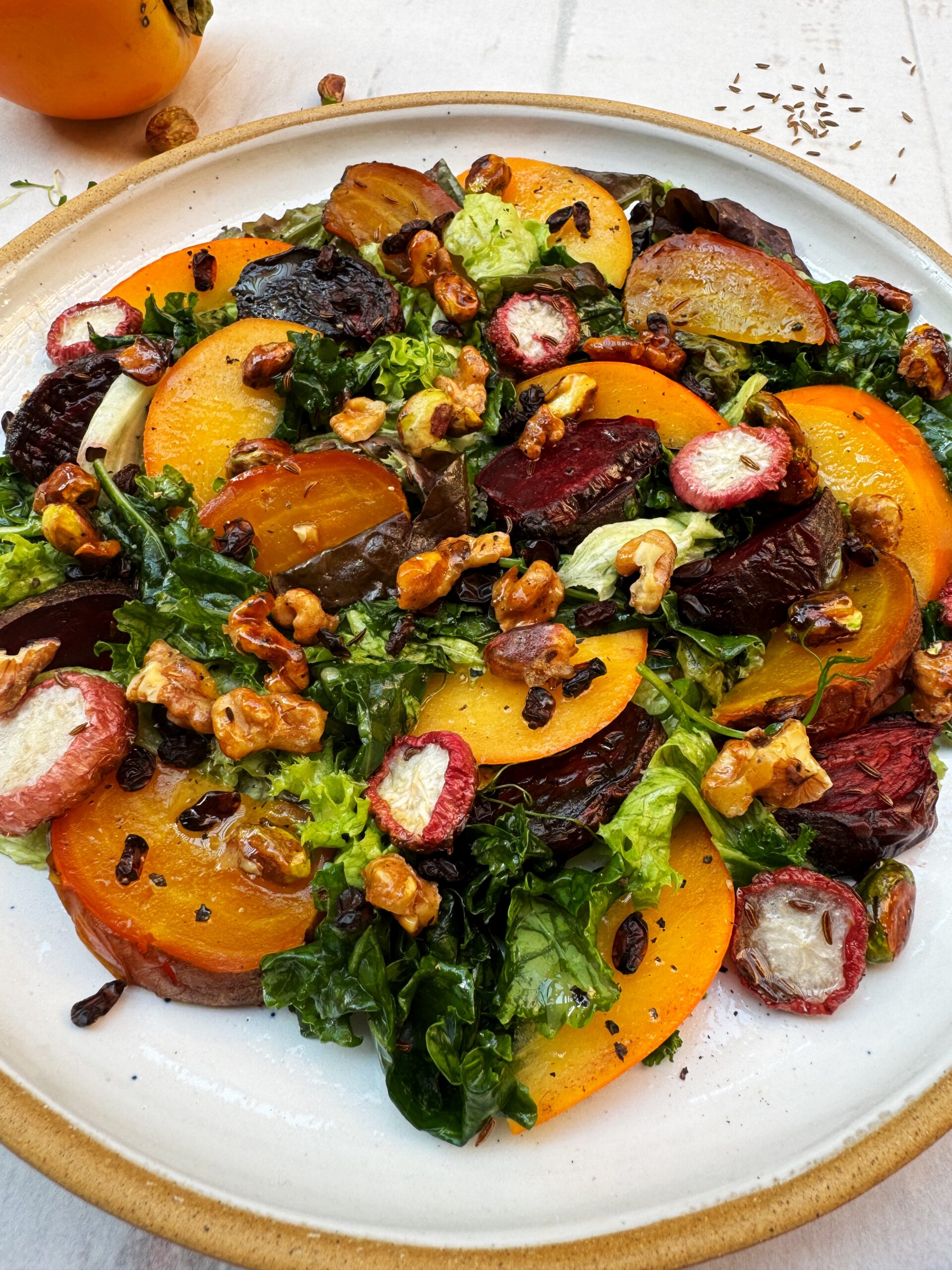 Slices of colorful roasted beets and fresh persimmons are mixed with salad greens and topped with candied nuts