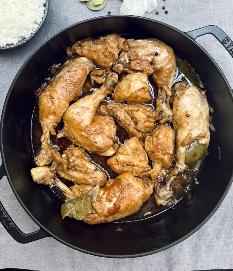 a casserole with pieces of chicken in a brown sauce with bay leaves and black peppercorns