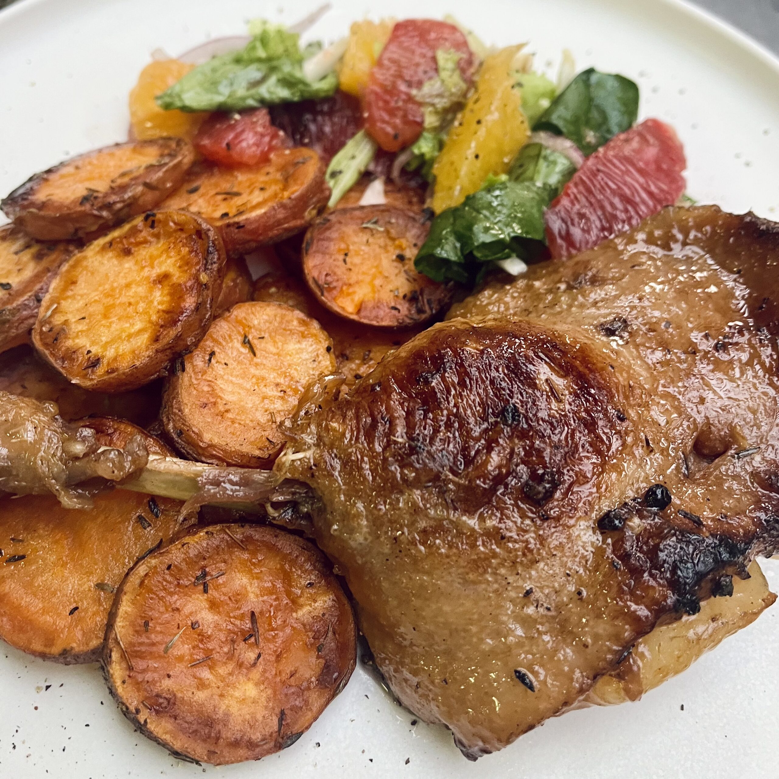 A leg of duck on a plate with roasted sweet potatoes and a citrus salad