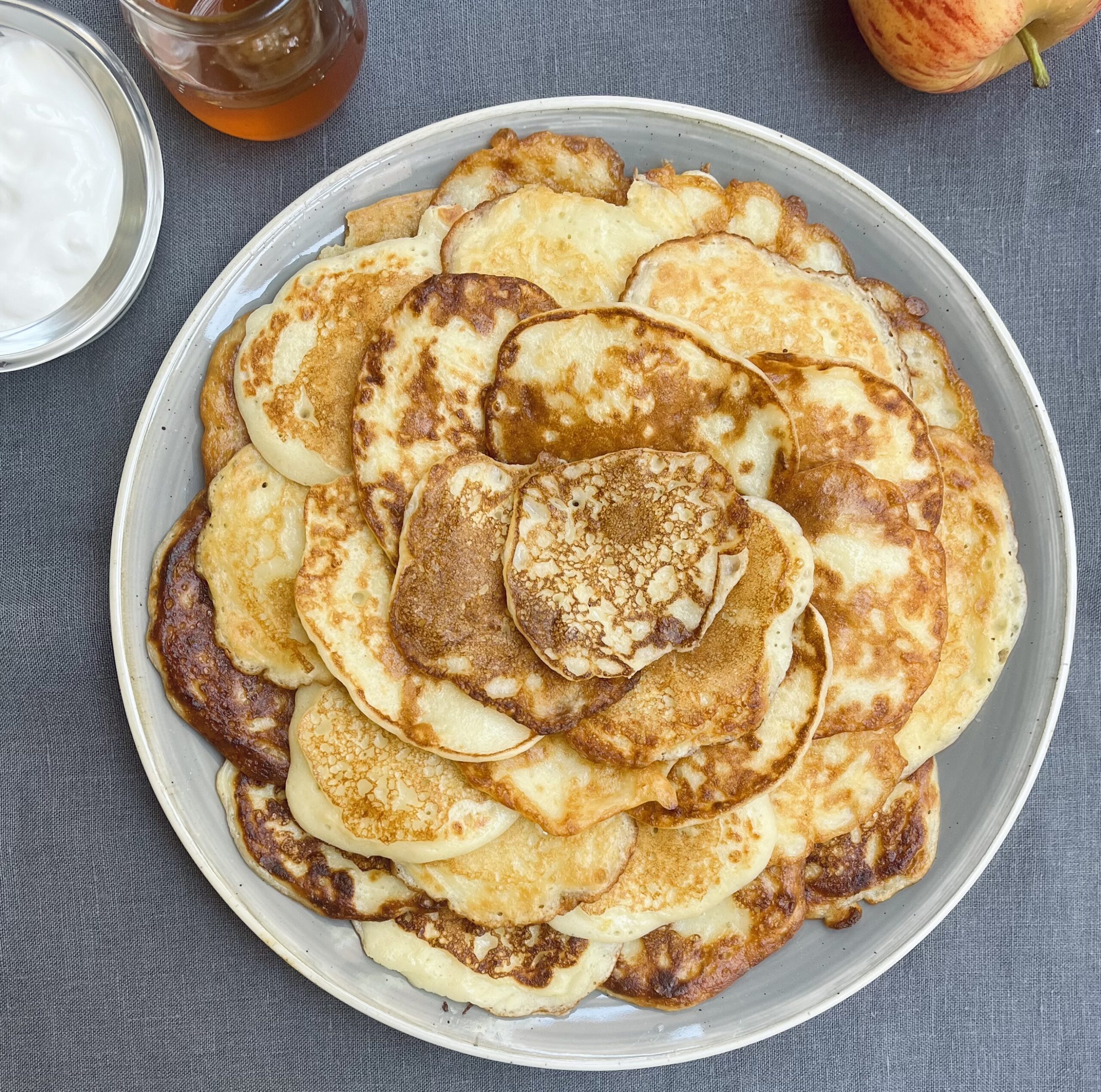 A neat pile of golden brown pancakes arrange on a light grey plate