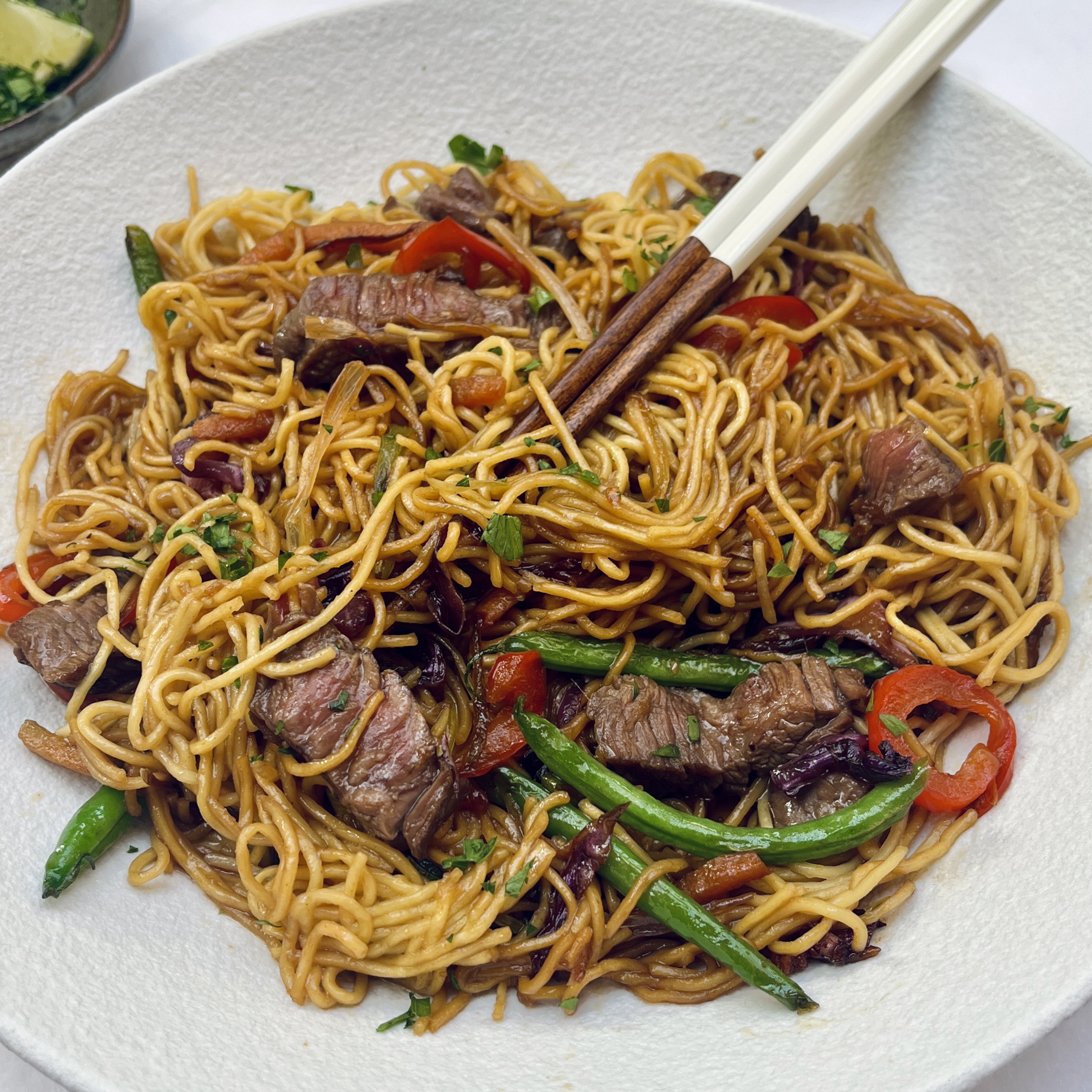 steak noodles in brown sauce with stir fried green and red vegetables and slices of steak cooked to medium