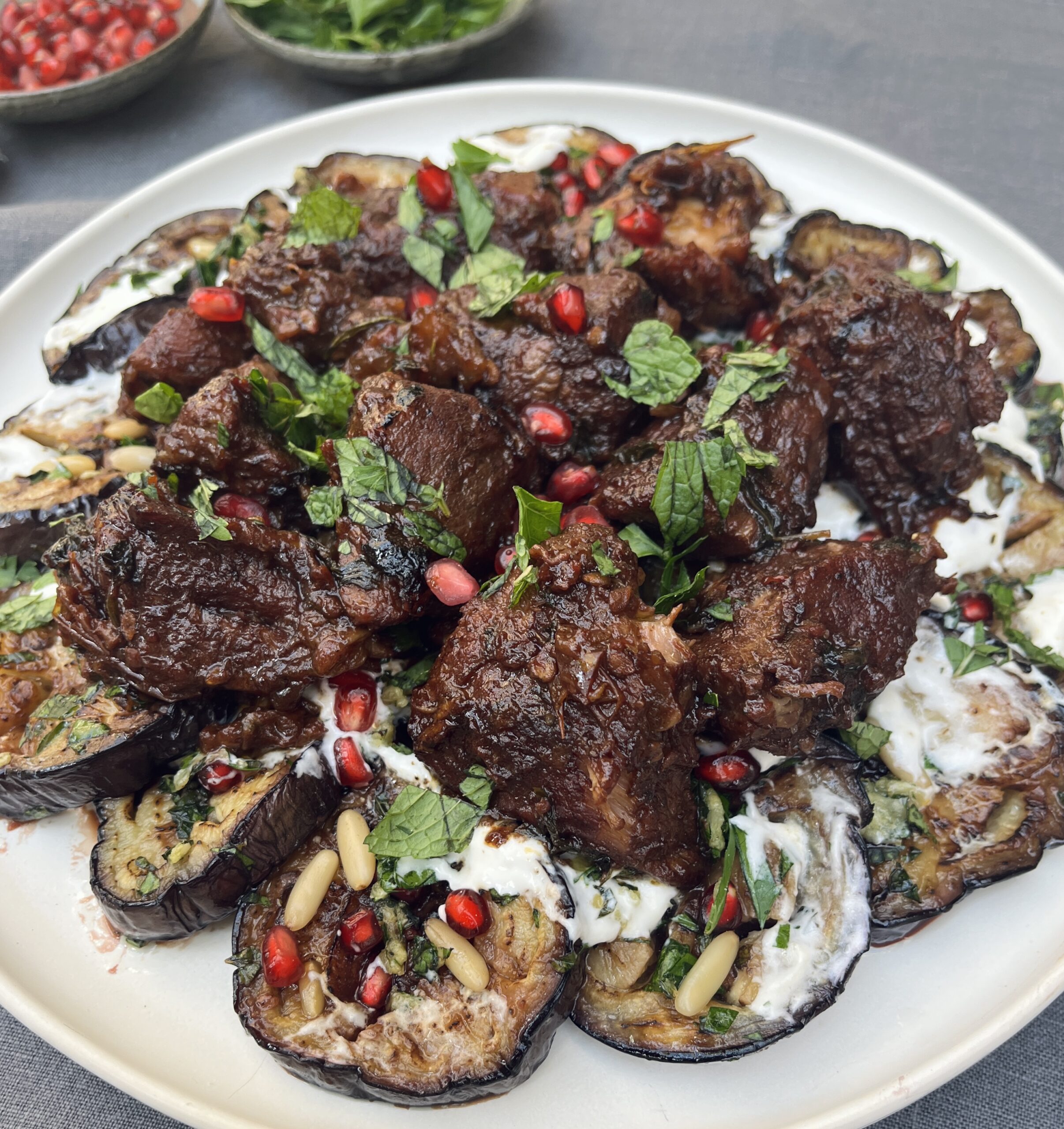 Braised veal lying on a plate decorated with fresh herbs and pomegranate jewels