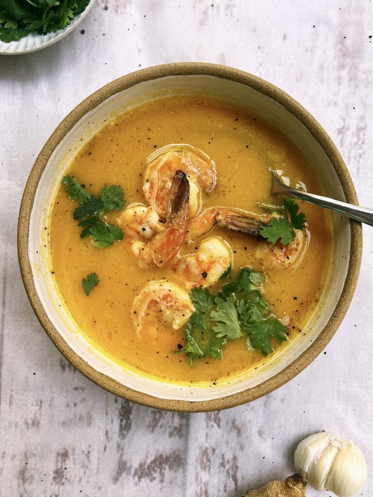 Orange smooth soup made from butternut squash and topped with cooked prawn and fresh coriander