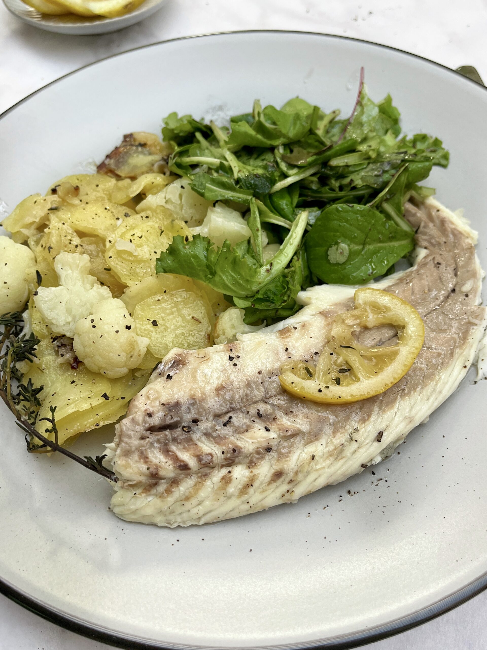 Seabass fillet topped with lemon served with potatoes and salad greens