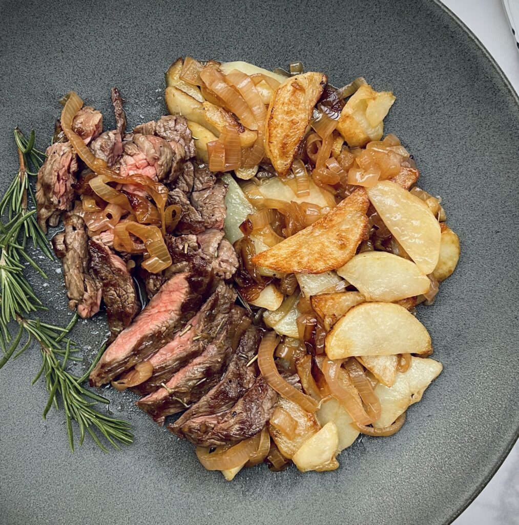 slices of steak bavette cooked to medium on a plate with fried potatoes and braised shallots