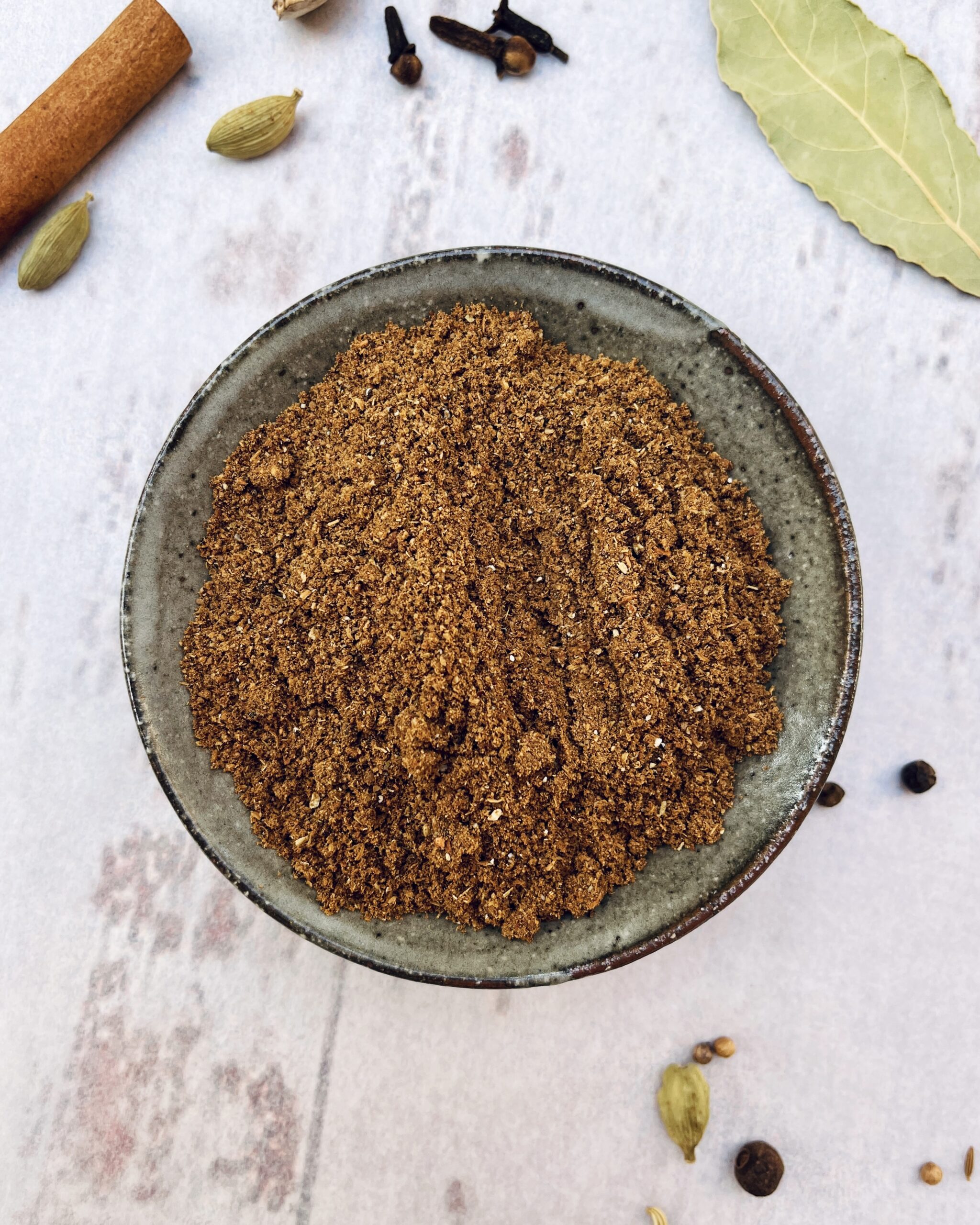 Garam masala blend on a small dish with whole spices scattered around