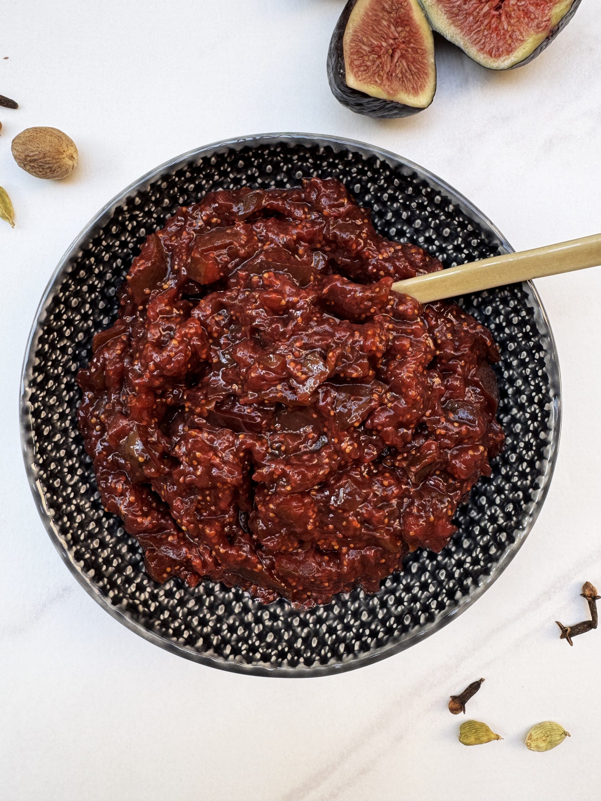 fig chutney in a dark grey bowl with a spoon dipped in