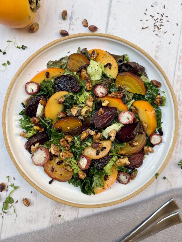 Roasted beets and persimmon salad is a colorful plate with red and golden roasted beets, small radishes and sliced persimmon mixed with salad greens and topped with candied nuts.