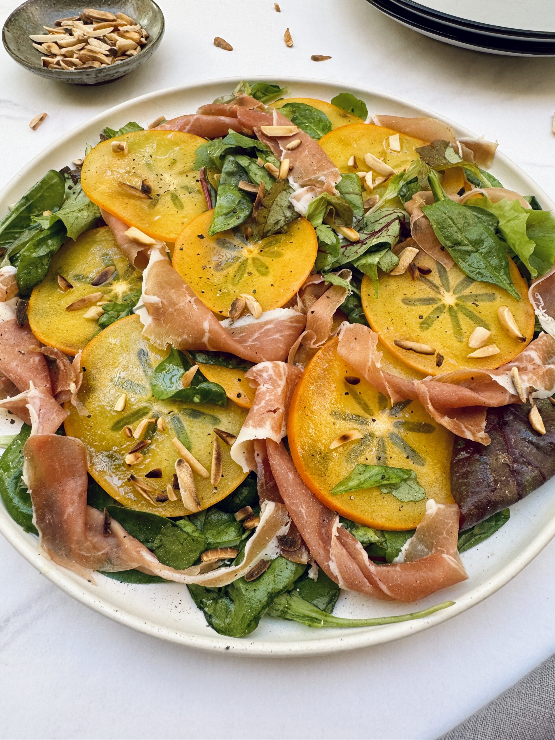 Salad greens with sliced persimmon and prosciutto topped with toasted almonds