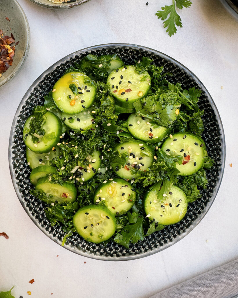 asian style salad with cucumber and kale with nuoc cham dressing, red chili flakes and sesame seeds