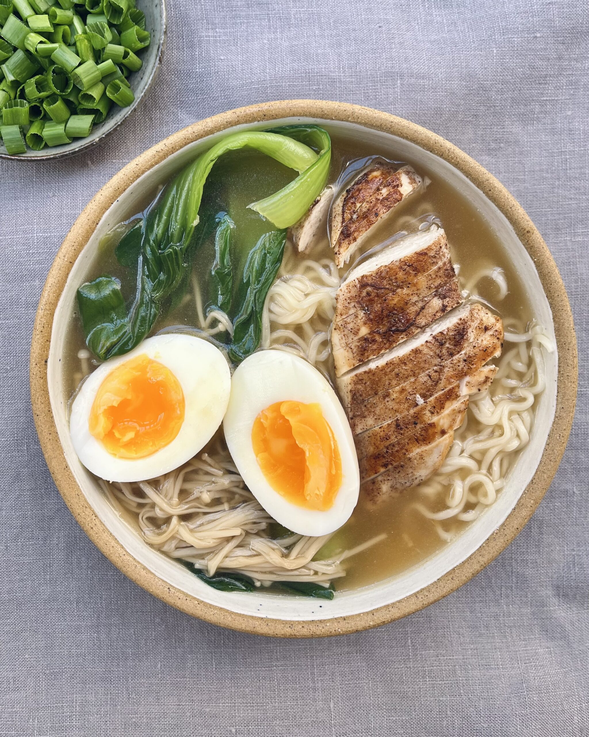 a bowl of chicken ramen noodles with sliced chicken breast, halved egg, pok choi and enoki muchrooms