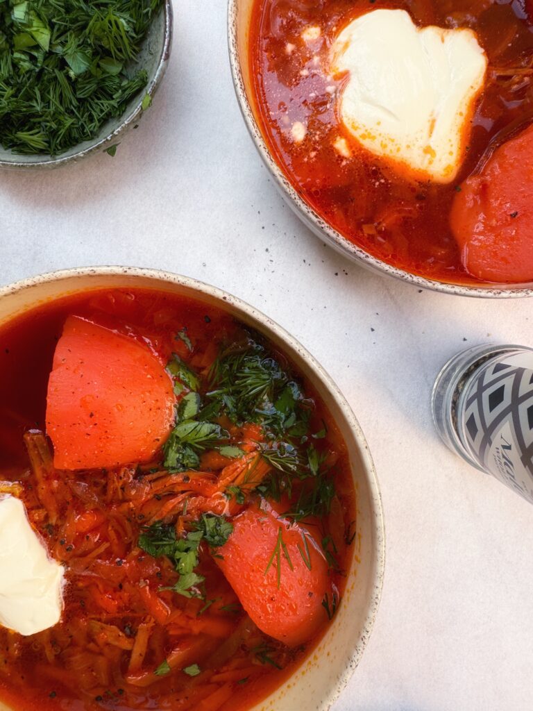 two plates with borscht, deep red colored soup with beetroot, potatoes, beef and fresh herbs