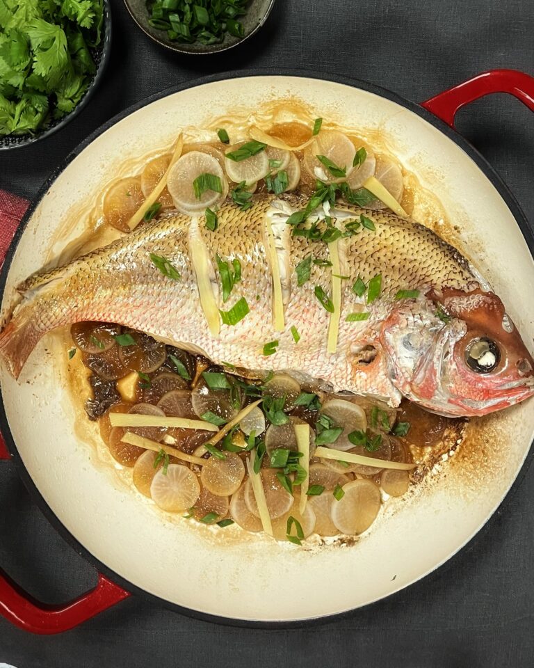 a whole red snapper in a large casserole with sliced daikon, ginger strips and scallions