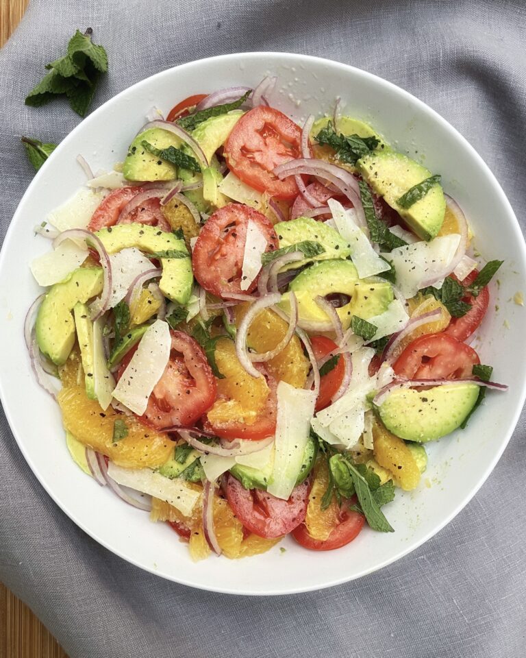 A plate of orange, tomato and avocado salad with sliced red onion, chopped mint and shaved manchego