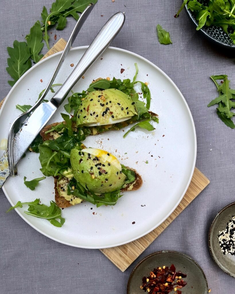 Egg in Avocado on a piece of toast bread with greens, red chili flakes and sesame seeds