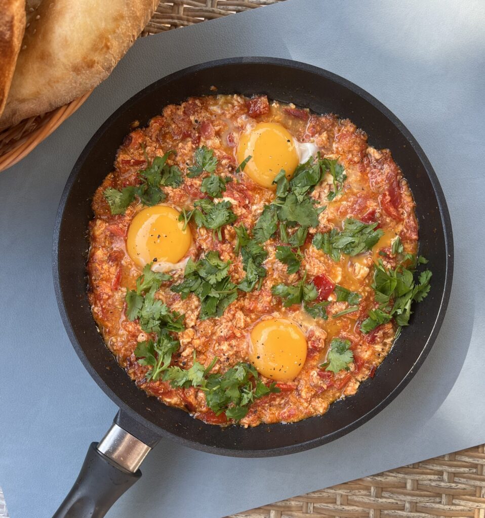 a pan with shakshuka with runny egg yolks in a rich red sauce topped with fresh coriander