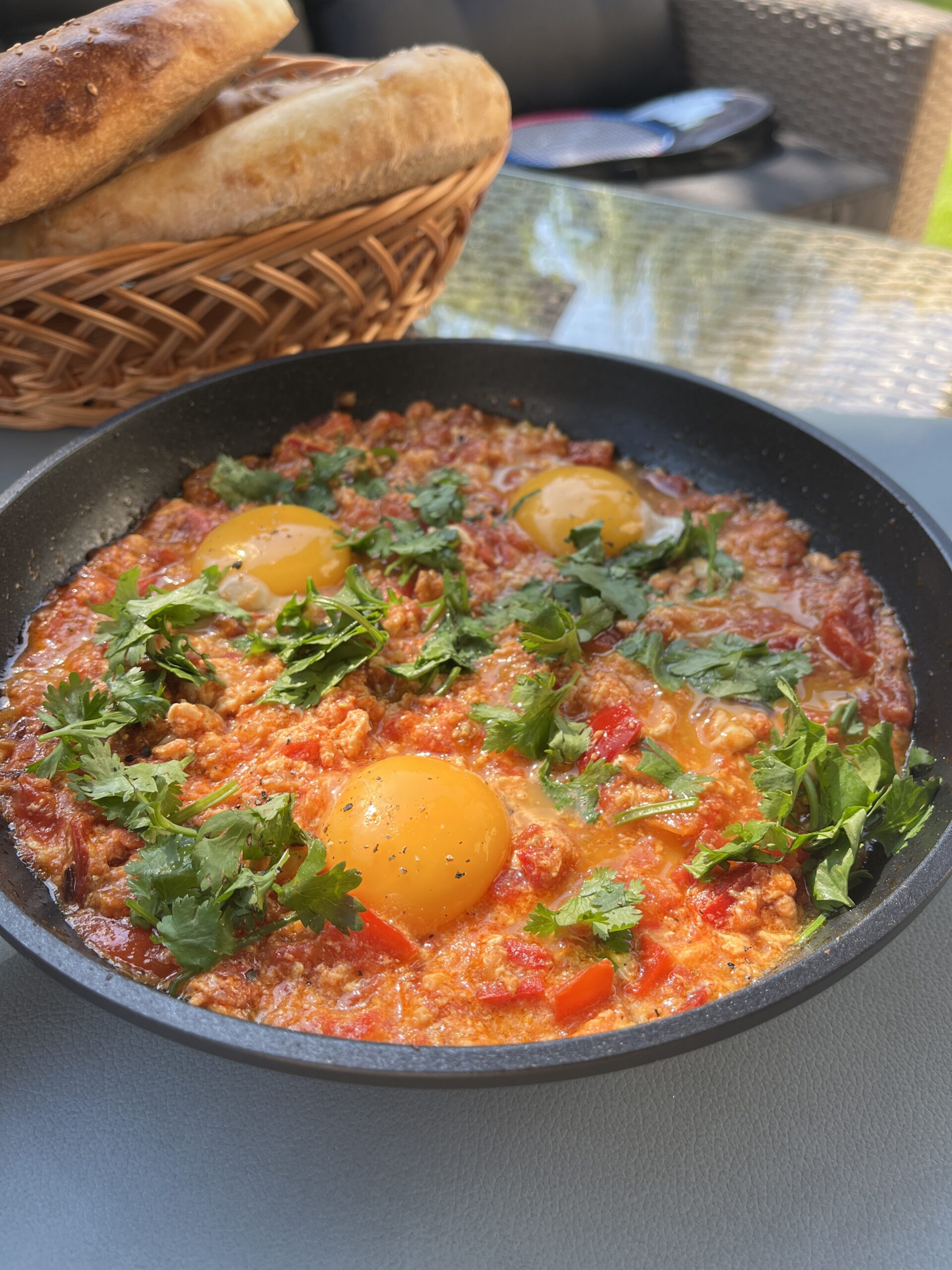 a pan with shakshuka with runny egg yolks in a rich red sauce topped with fresh coriander