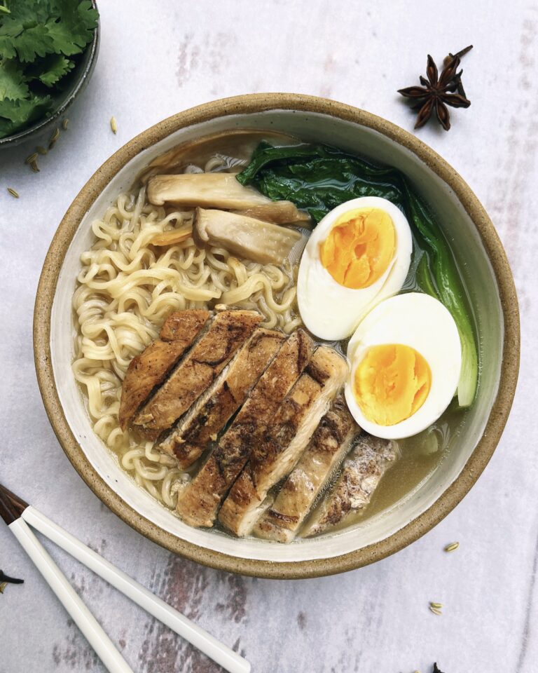 A bowl with chicken ramen containing ramen noodles, spiced chicken breast, egg, slcied mushrooms and pak choi