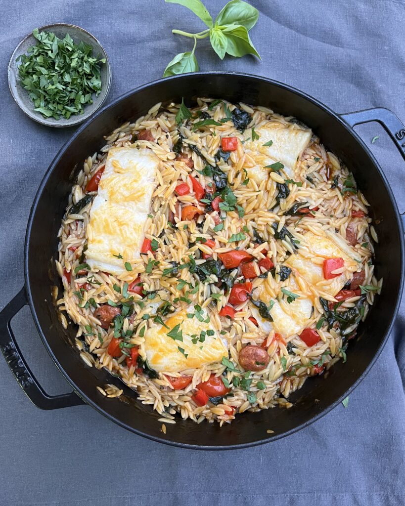 a casserole with orzo pasta, white fish, chorizo, red bell peppers and fresh herbs