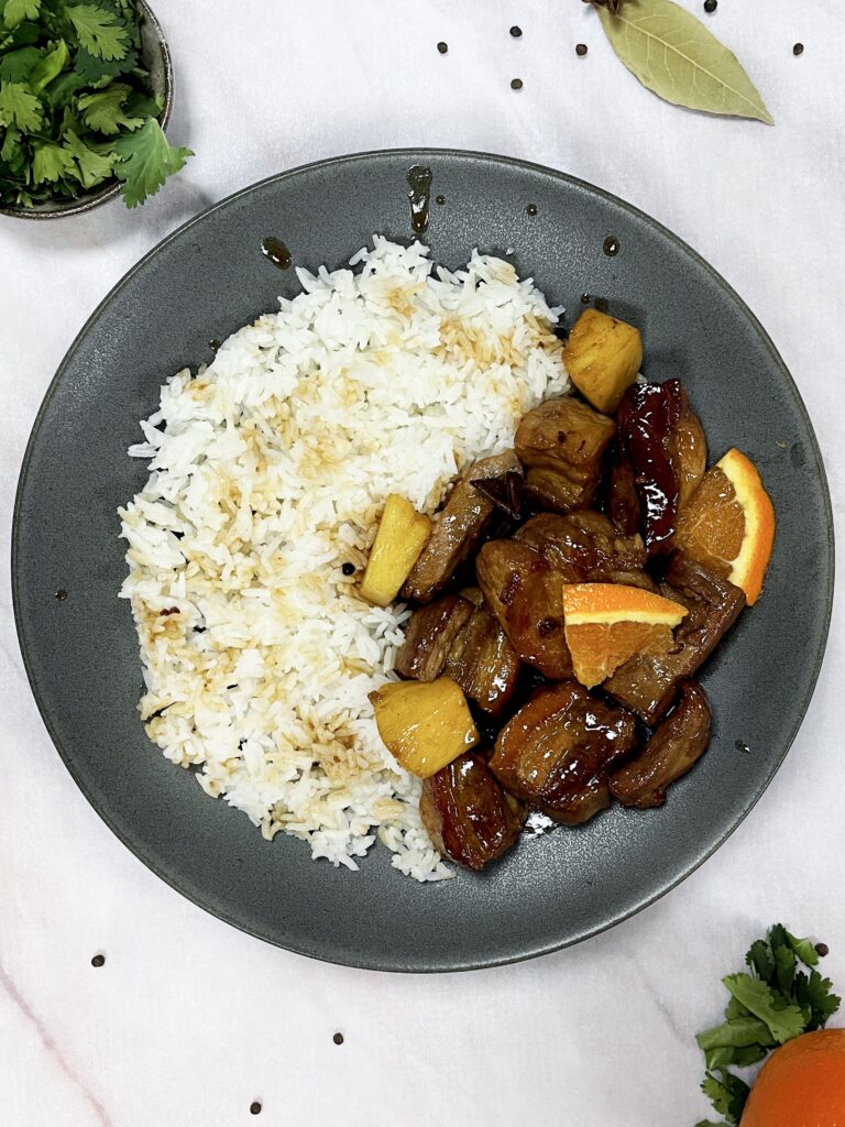 a plate with white rice and chunks of sticky pork belly covered in a glossy glaze with pieces of orange and pineapple