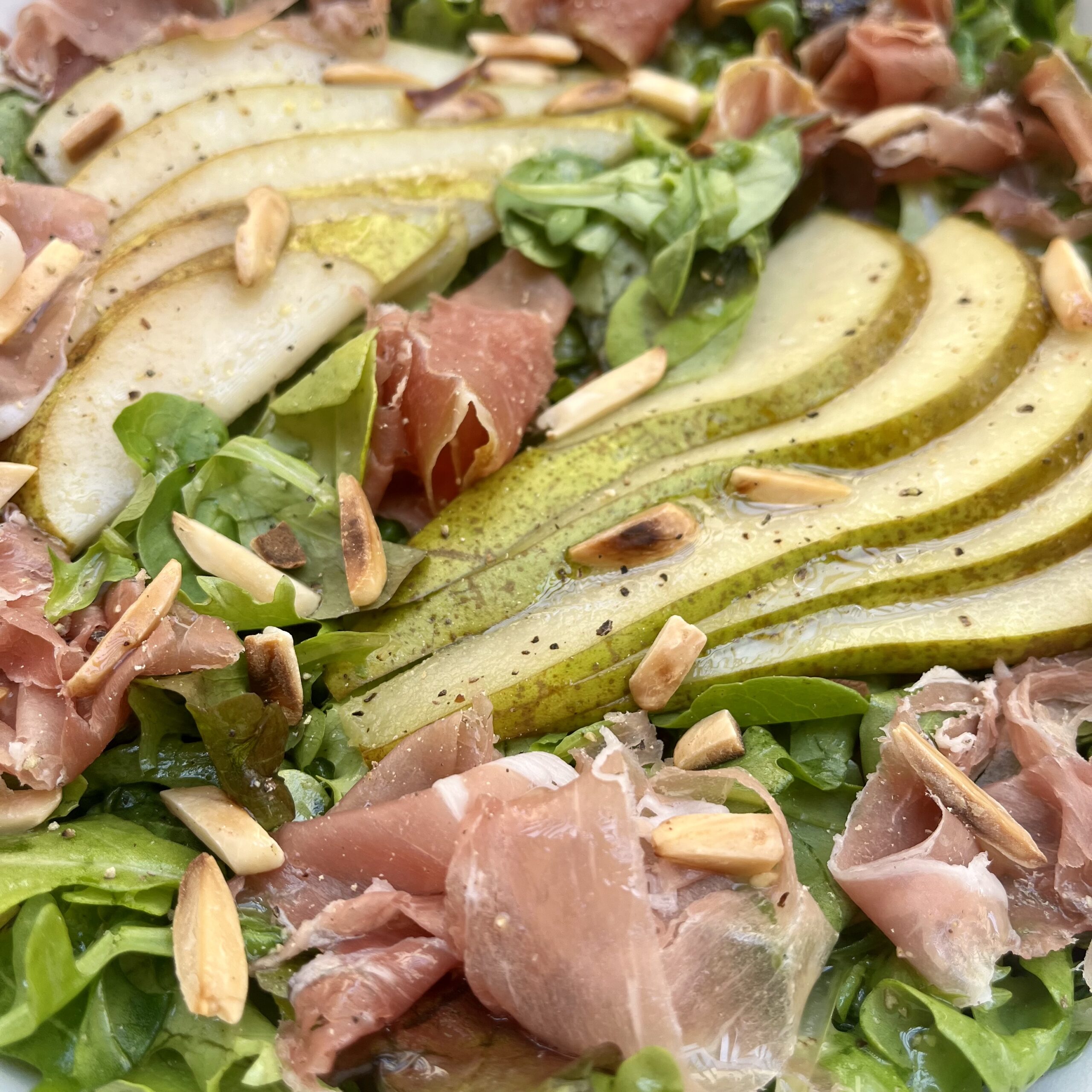 Sliced Conference Pear and slices of Prosciutto over a bed of rocket leaves garnished with roasted almonds