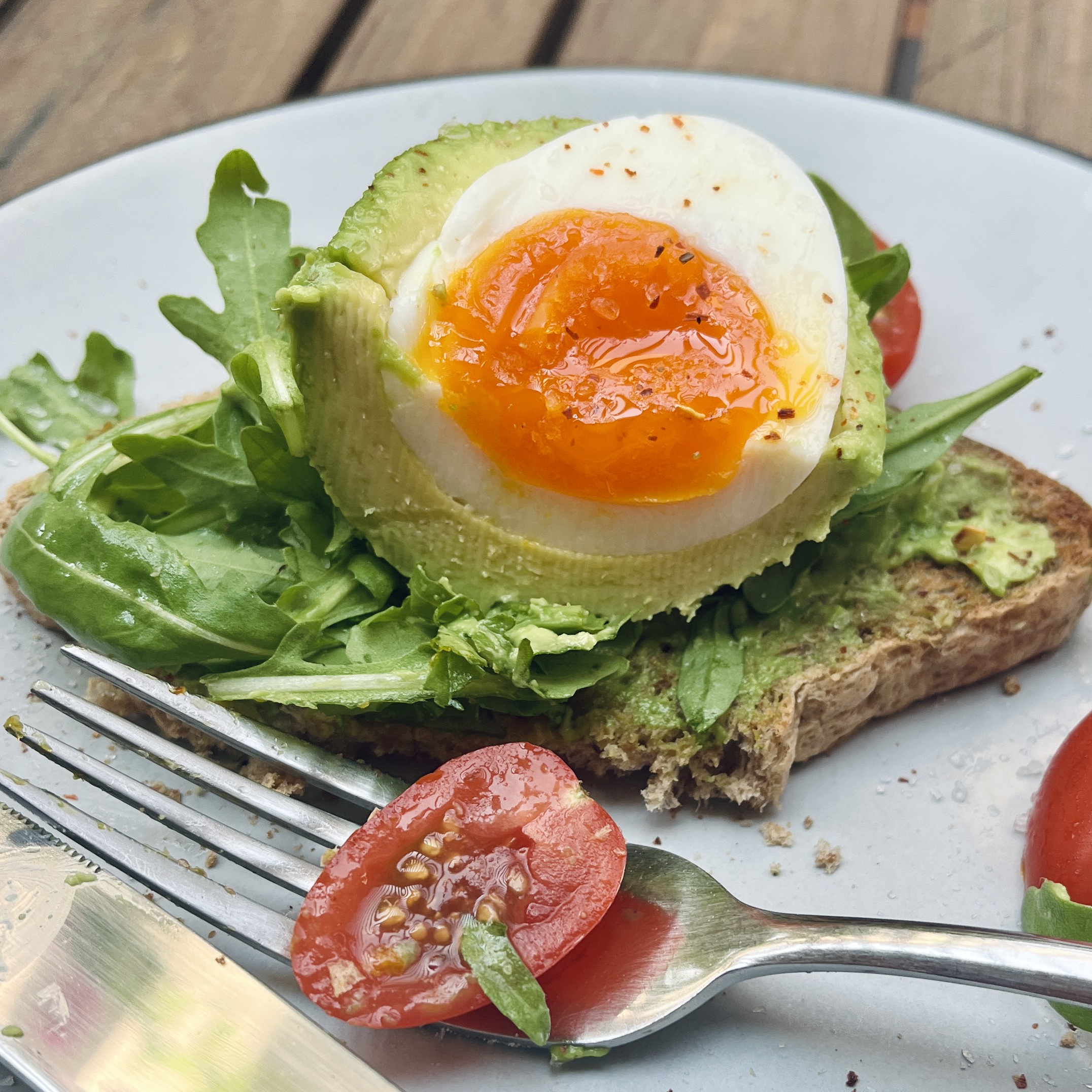 Egg in Avocado on a piece of toast bread with greens, red chili flakes and sesame seeds