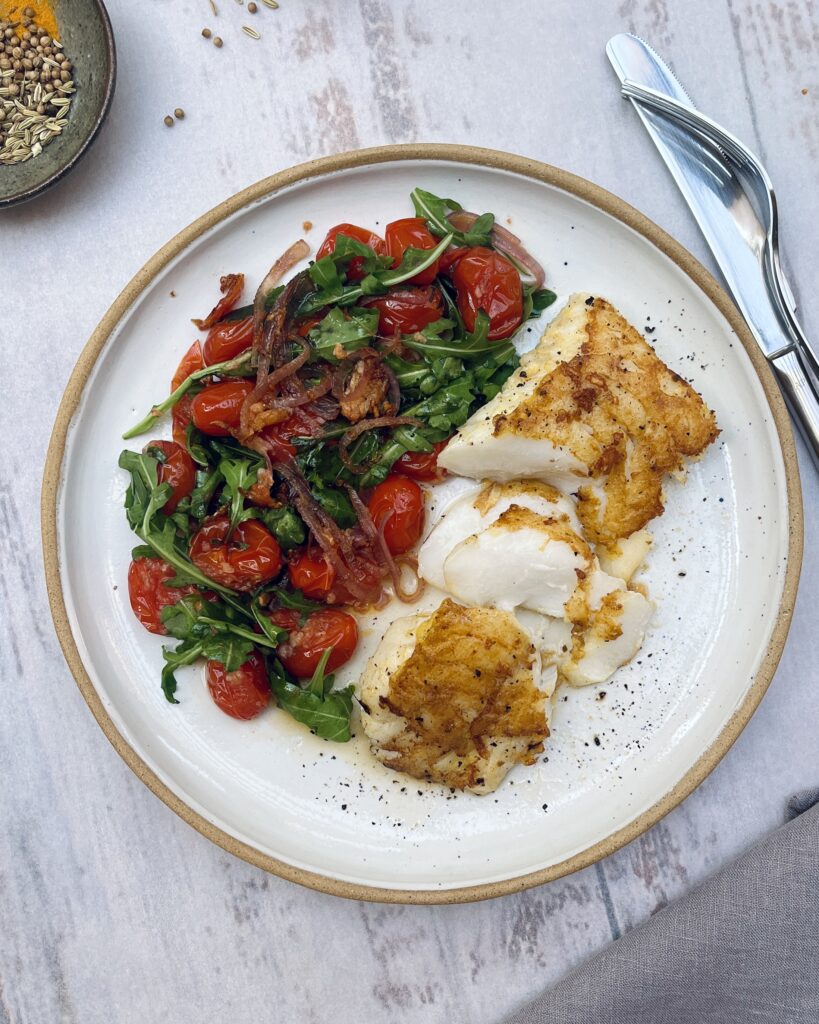 Flaky cod in golden batter alongside ruccola and tomato salad