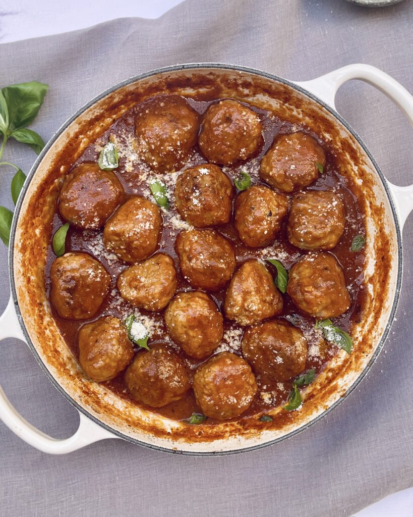 A casserole with meatballs in red tomato sauce sprinkled with grated parmesan