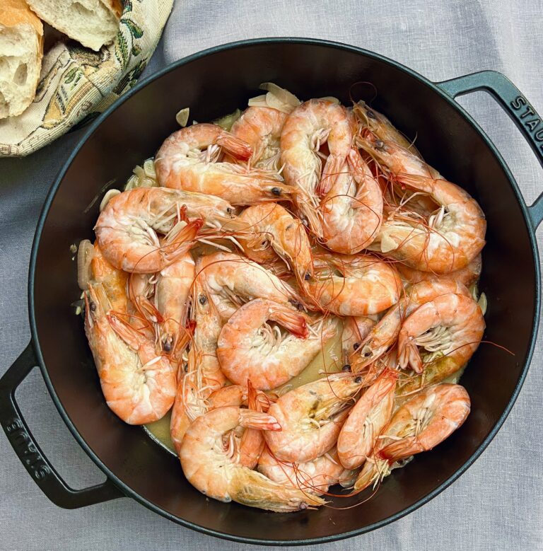 large black casserole with whole cooked prawns in a buttery sauce