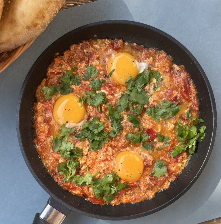 a pan with shakshuka with runny egg yolks in a rich red sauce topped with fresh coriander