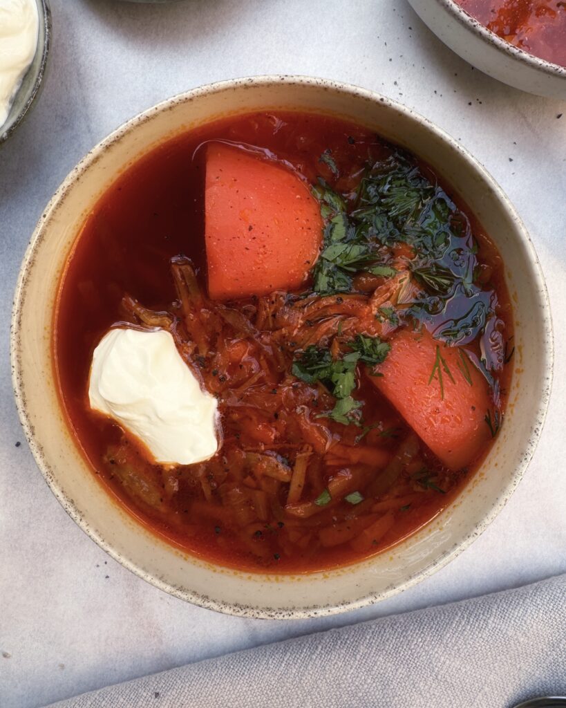 deep red colored borscht soup with beetroot, potatoes, beef and fresh herbs, topped with sour cream