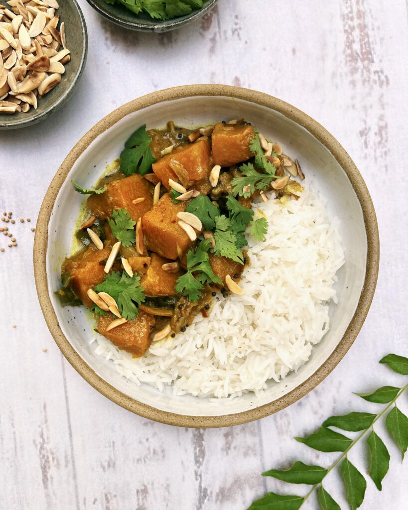 Pumpkin curry with chunks of pumpkin cooked with spices and aromatics and topped with toasted almonds and fresh coriander alongside white rice