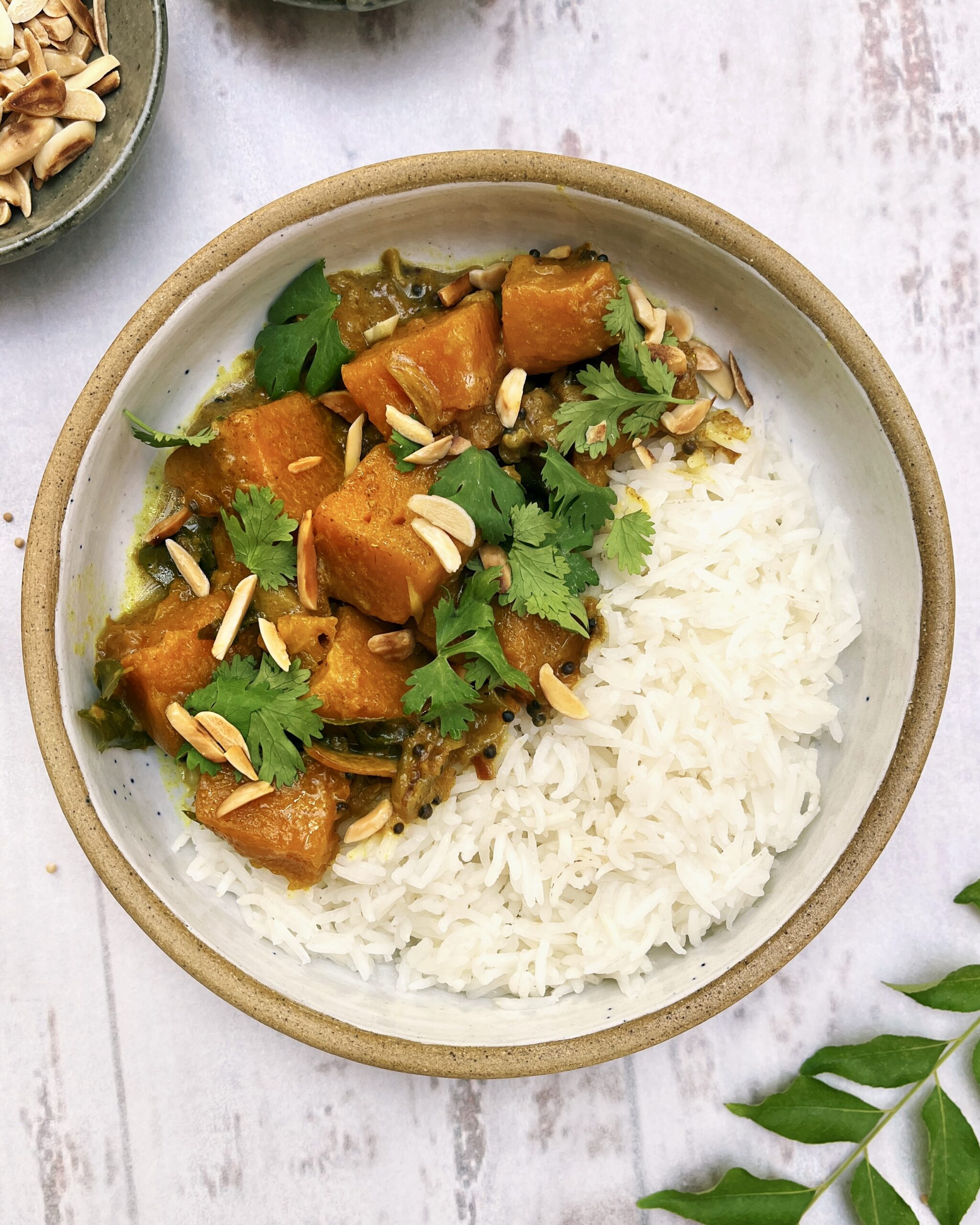 Pumpkin curry with chunks of pumpkin cooked with spices and aromatics and topped with toasted almonds and fresh coriander alongside white rice