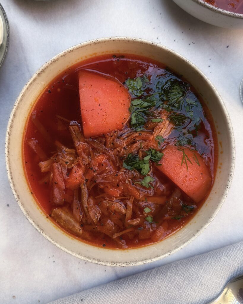 deep red colored borscht soup with beetroot, potatoes, beef and fresh herbs