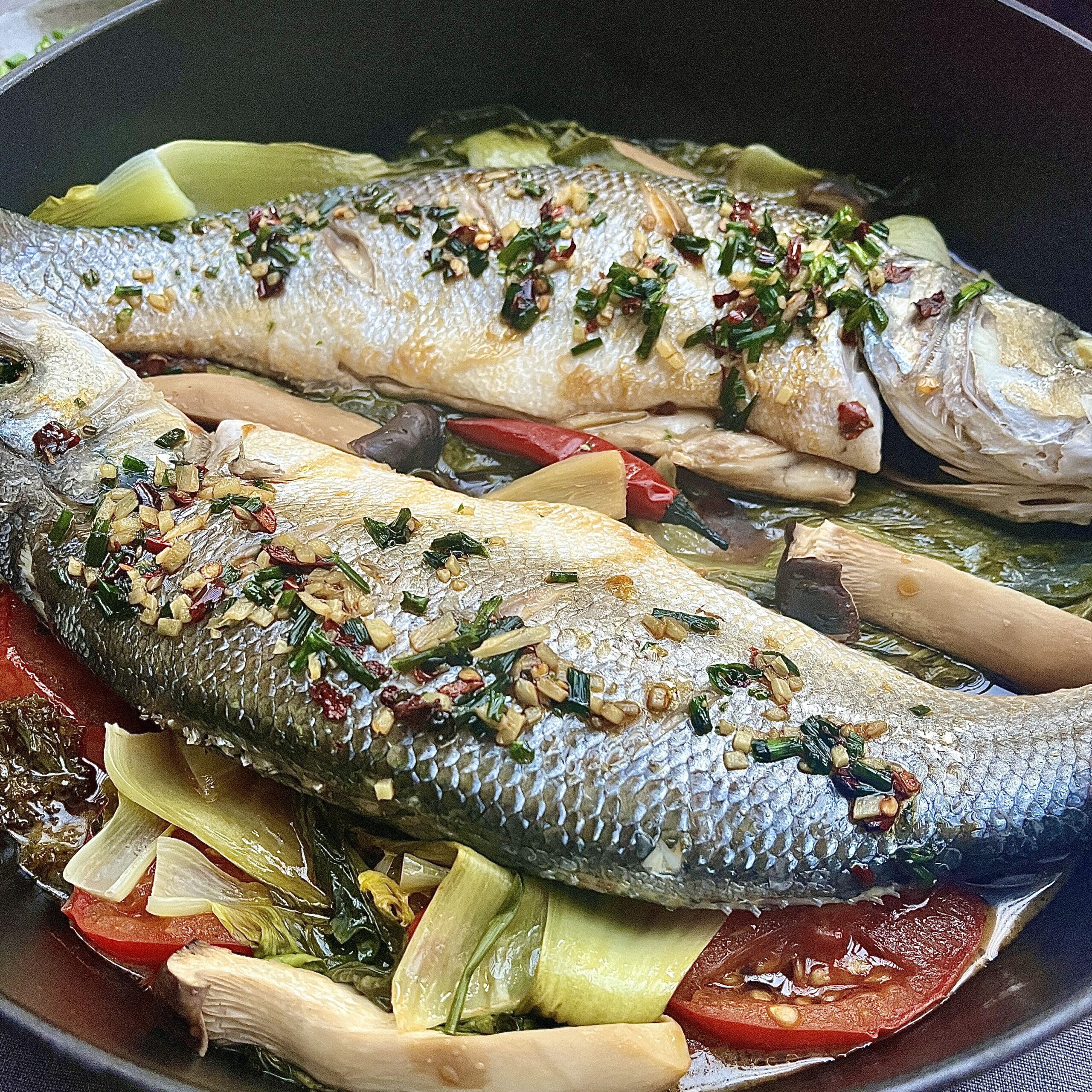 who sea bass with silver skin is lying over a bed of colorful vegetables.