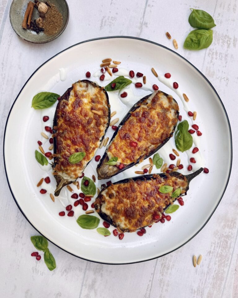 A plate with halves of Stuffed Eggplant topped with melted cheese, basil leaves, pine nuts and pomegranate seeds, Dinner Categories, Beef