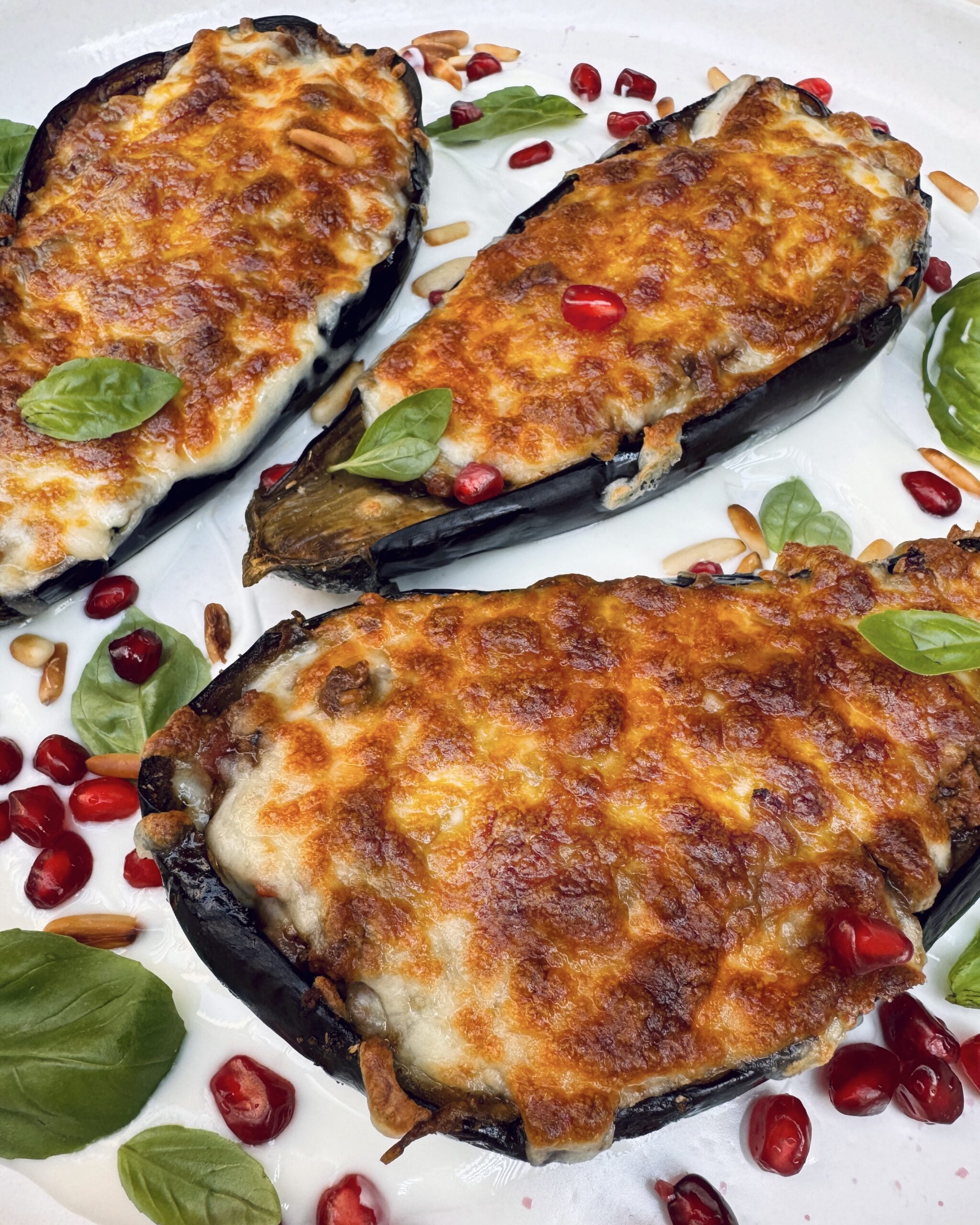 Eggplant topped with melted cheese, basil leaves, pine nuts and pomengranate seeds