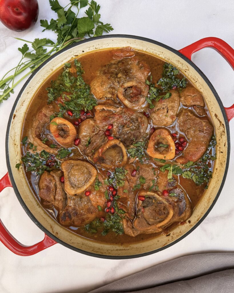 Braised Veal Shanks in a red sauce made with tkemali and tomatoes garnished with fresh herbs and pomegranate jewels