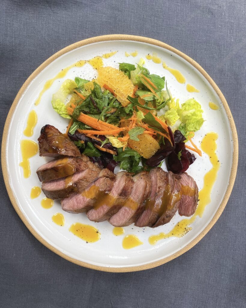 Sliced duck breast with a drizzle of orange dressing alongside a zesty salad