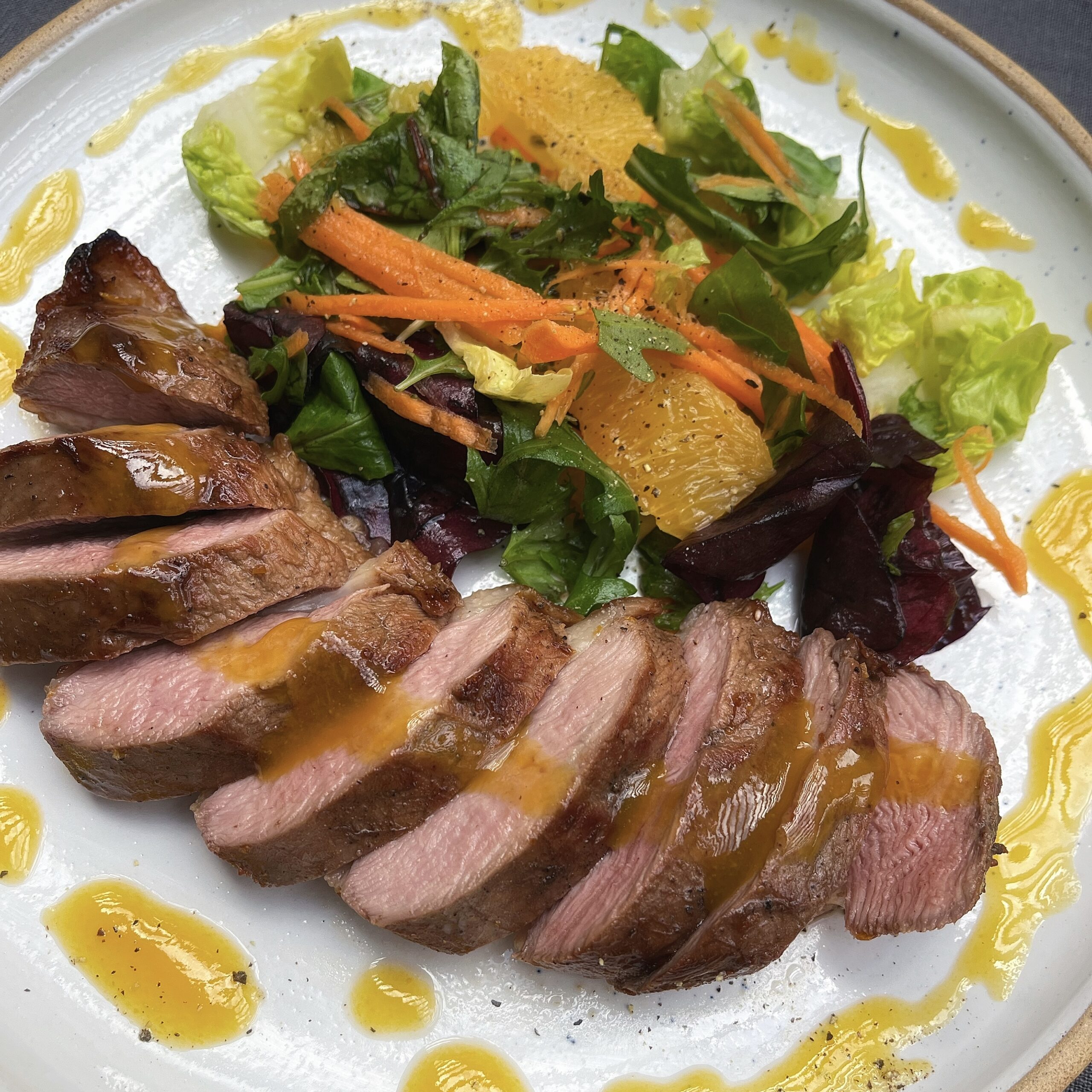 Sliced duck breast with a drizzle of orange dressing alongside a zesty salad