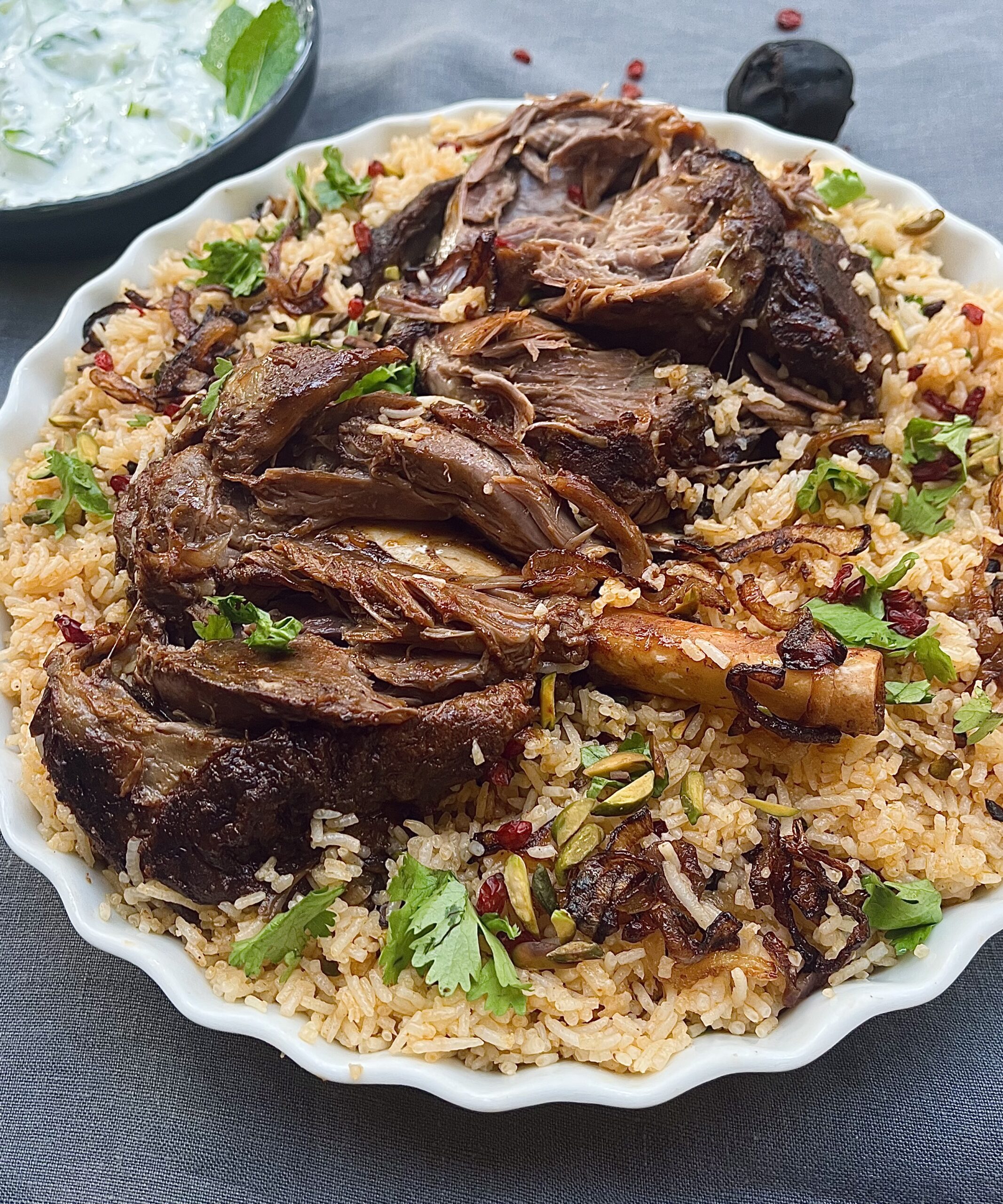 Roasted lamb shanks over a bed of spiced rice garnished with pistachios, pomegranate seeds, barberries and coriander leaves