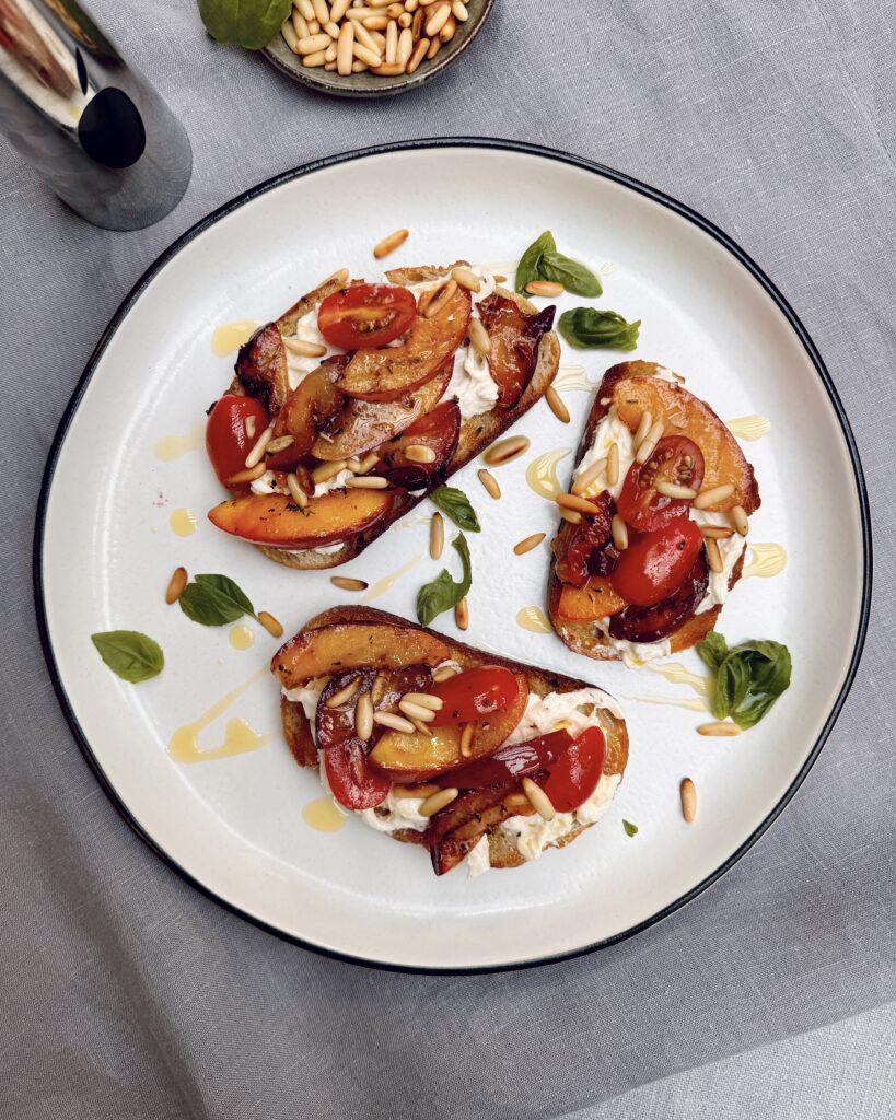 A plate with colorful Sourdough toast with grilled nectarine and burrata with cherry tomatoes, pine nuts and basil