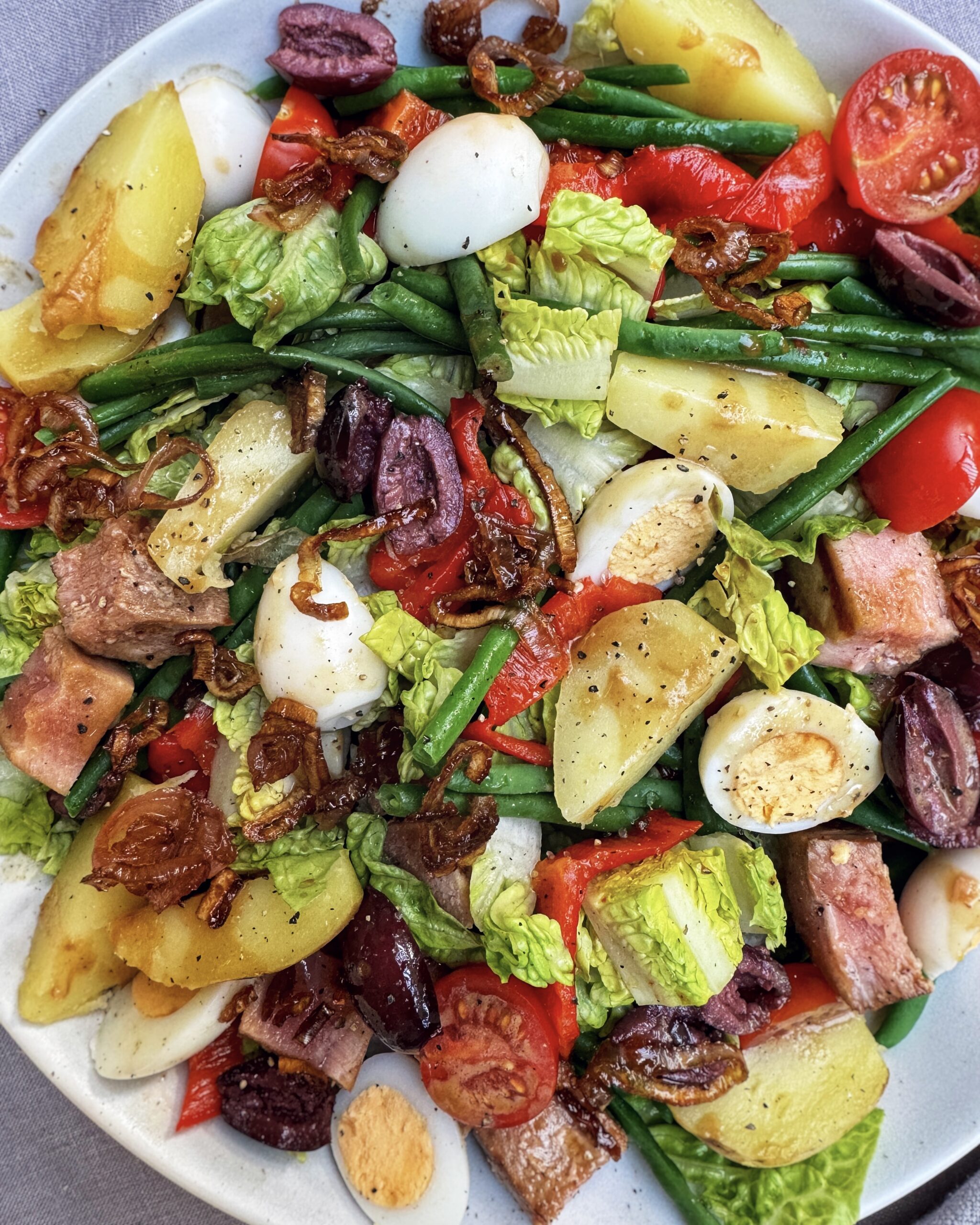 nicoise salad with lettuce, tomatoes, green beans, potatoes, eggs, olives, caramelized onions and roasted bell peppers