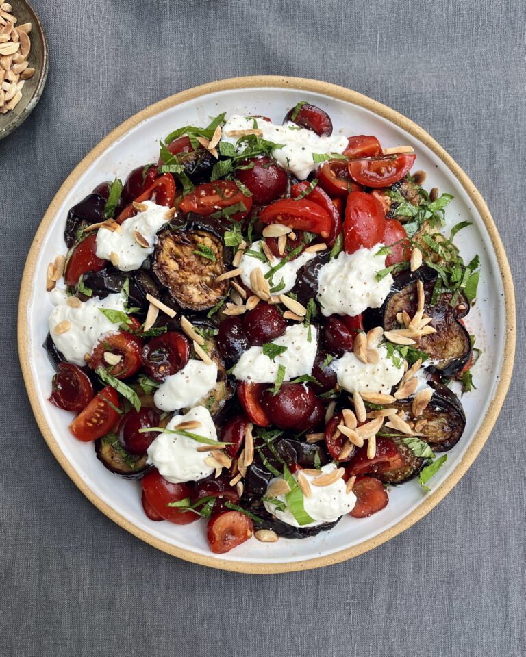 A plate of fried eggplant with marinated cherries, burrata, fresh herbs and roasted almonds