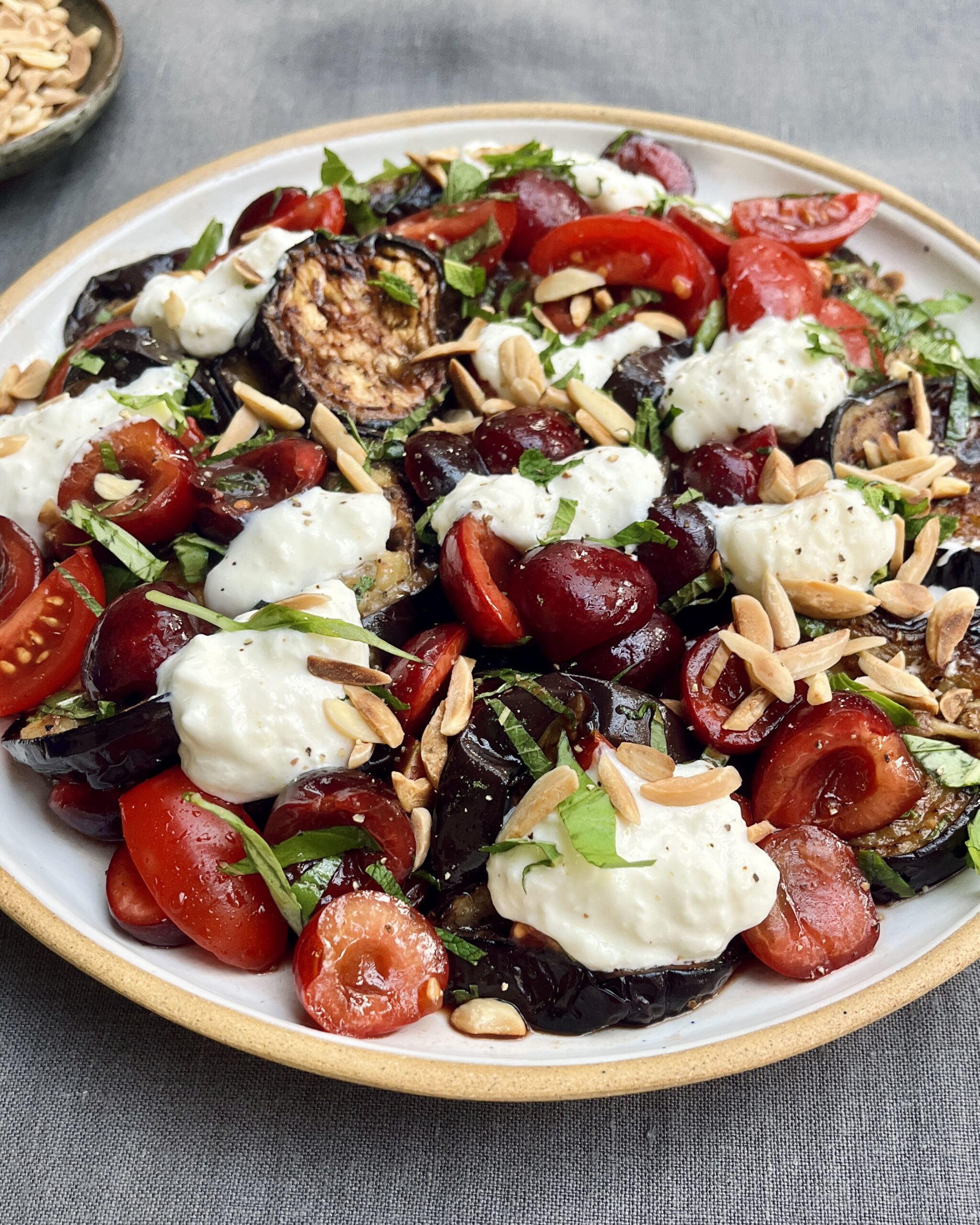 A plate of fried eggplant with marinated cherries, burrata, fresh herbs and roasted almonds.