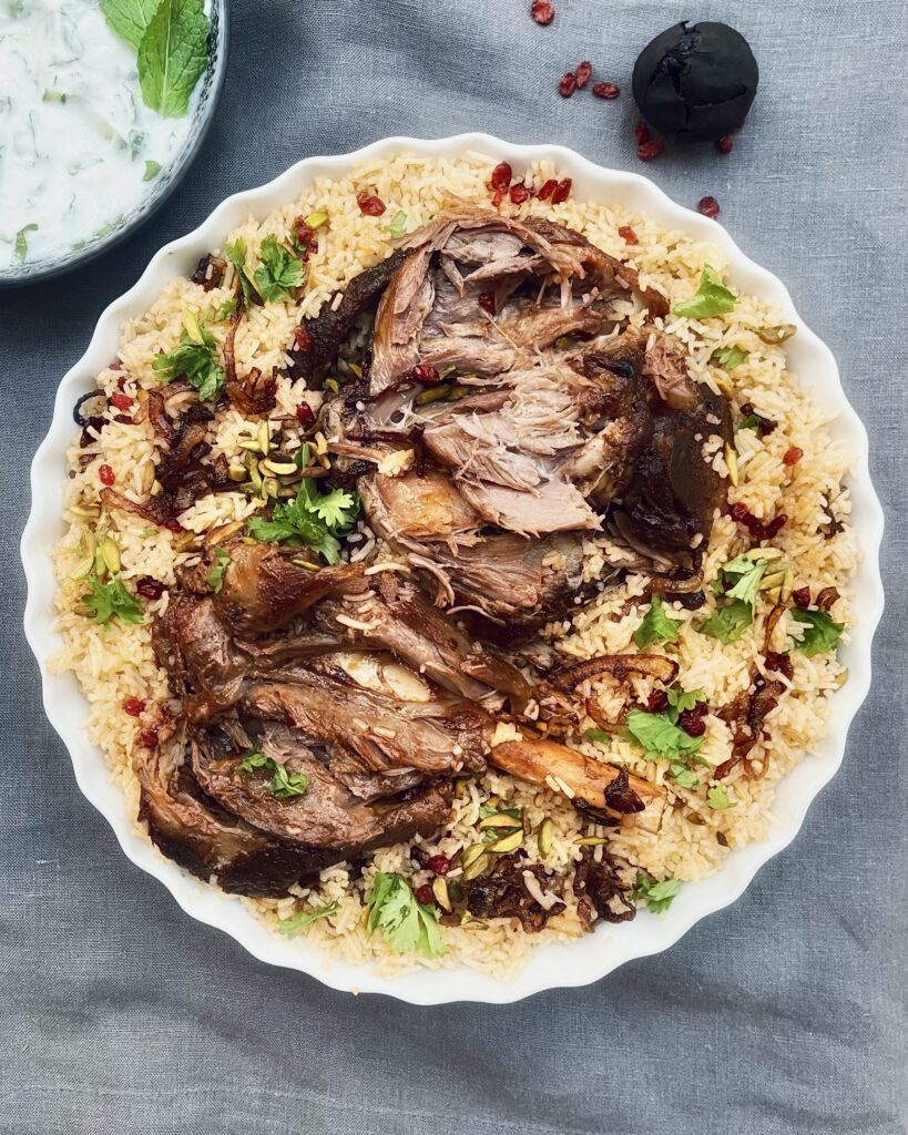 Roasted lamb shanks over a bed of spiced rice garnished with pistachios, pomegranate seeds, barberries and coriander leaves