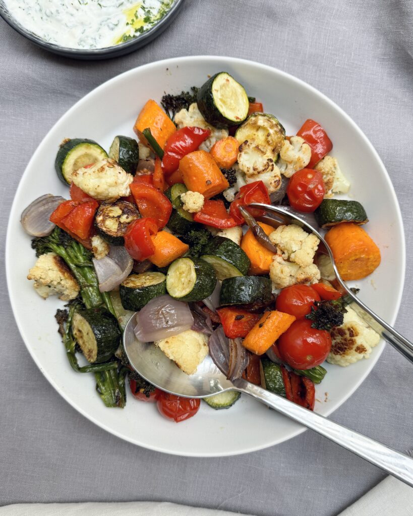 A plate with colorful mixed roasted vegetables with a side of fresh yoghurt