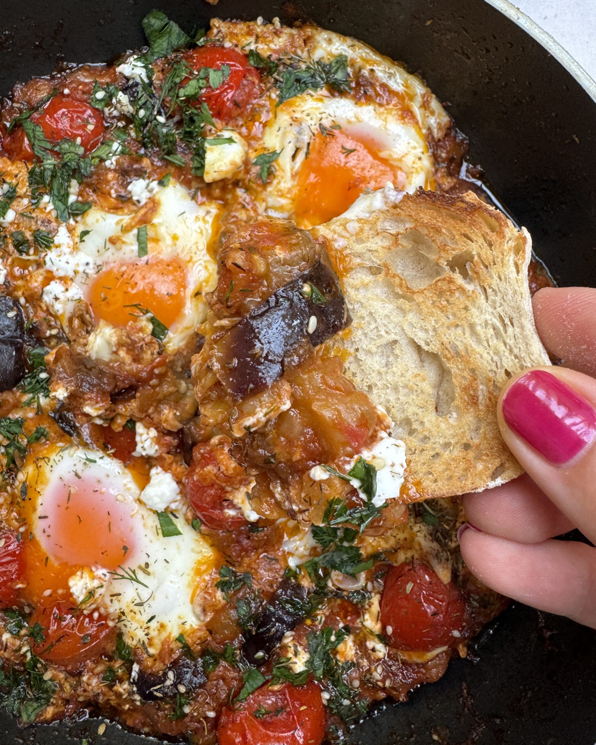 crusty piece of bread goes into eggplant shakshuka topped with crumbled feta, fresh herbs and zaatar