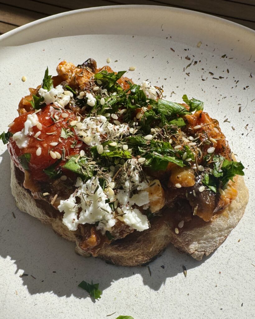 a piece of toast with shakshuka sauce on it, topped with crumbled feta and fresh herbs